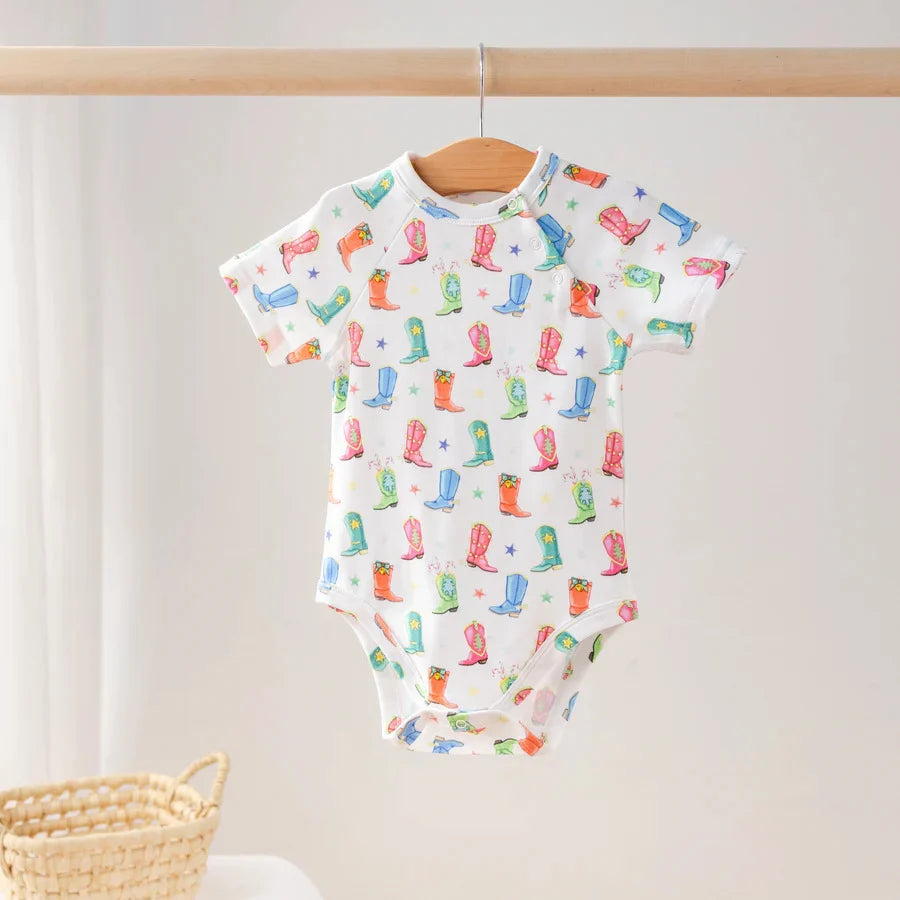 White short-sleeve baby bodysuit with colorful cowboy boots and stars, hanging on a wooden hanger.